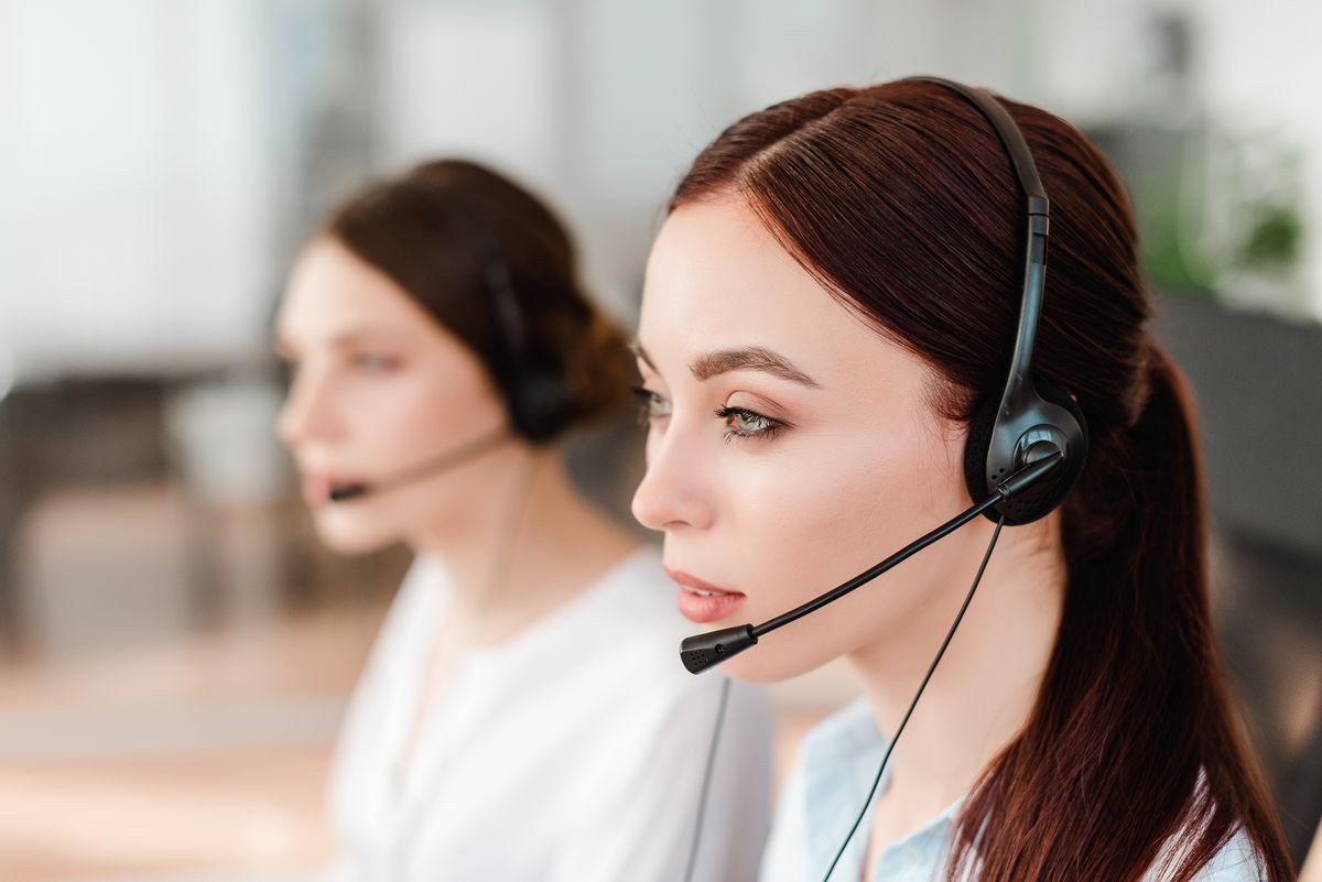 Concentrated young office worker with a headset  answering in a call center, woman talking with clients. Portrait of an attractive customer and technical support representative. Business concept