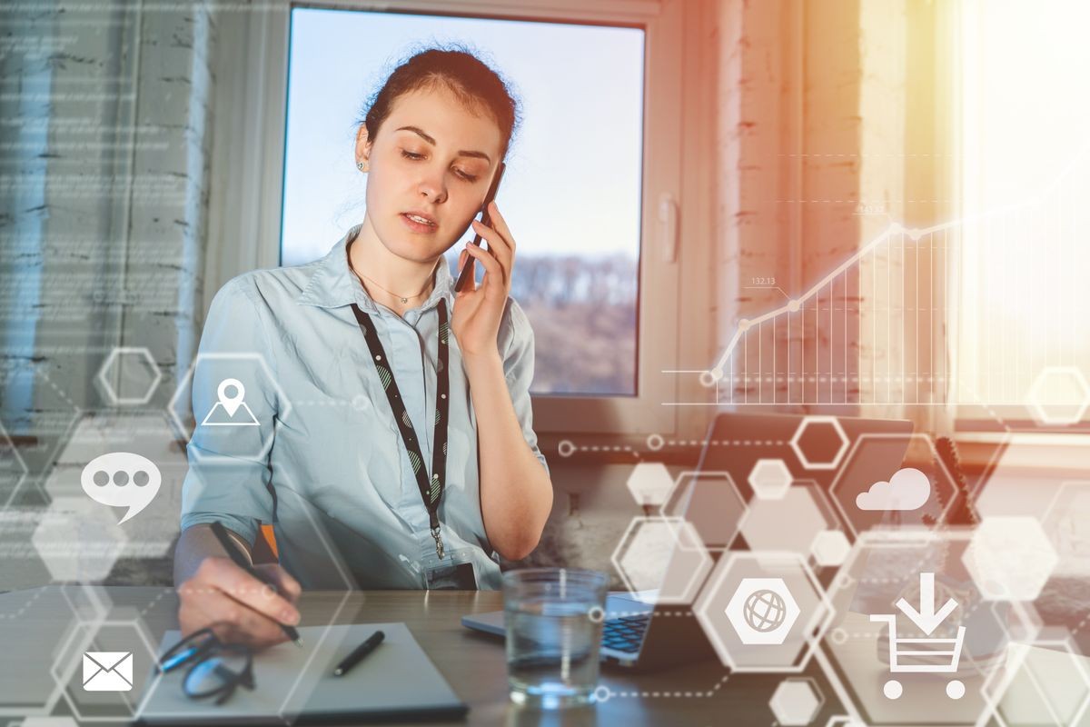 Young attractive casually dressed female entrepreneur answering a call in the office on her mobile phone. Work in process. Virtual futuristic background with various applications icons.